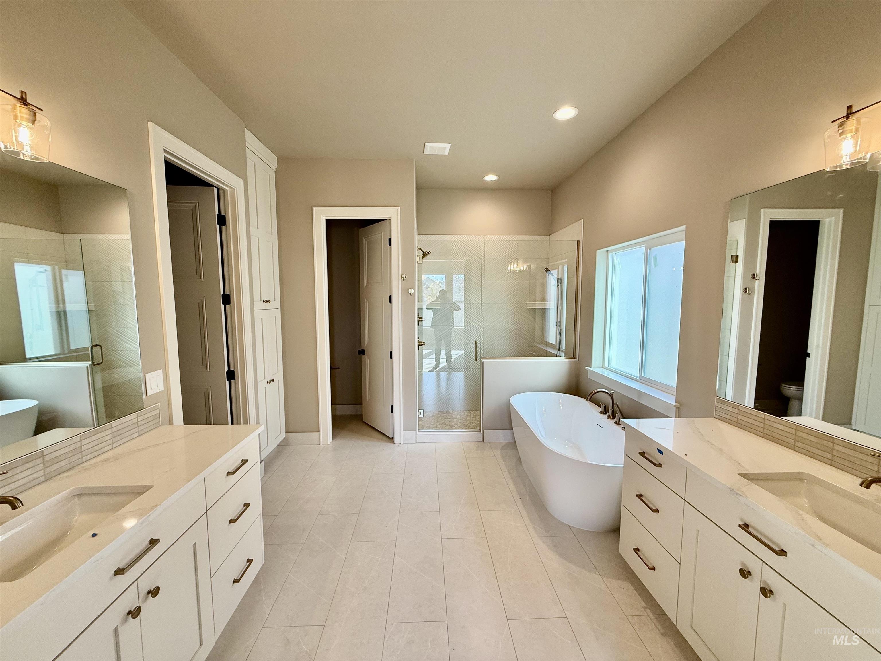 Full bath featuring a freestanding bath, a shower stall, two vanities, recessed lighting, and light tile patterned flooring