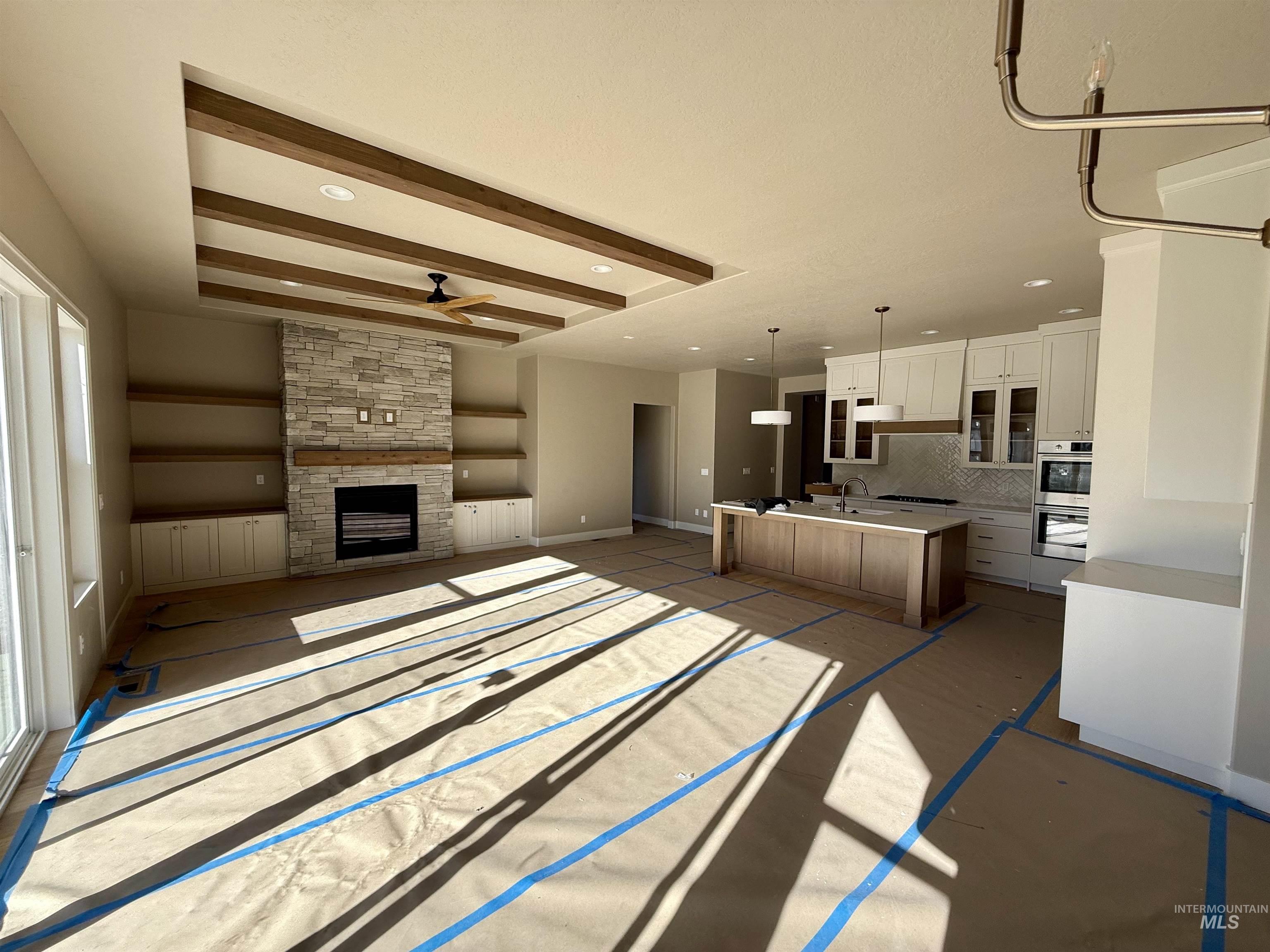 Unfurnished living room featuring beamed ceiling, ceiling fan, a stone fireplace, and recessed lighting