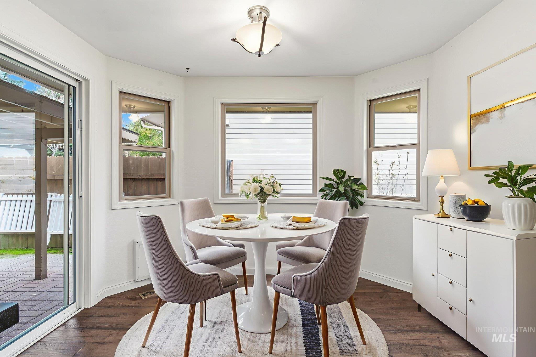 Virtually staged dining room with dark wood-style floors and healthy amount of natural light