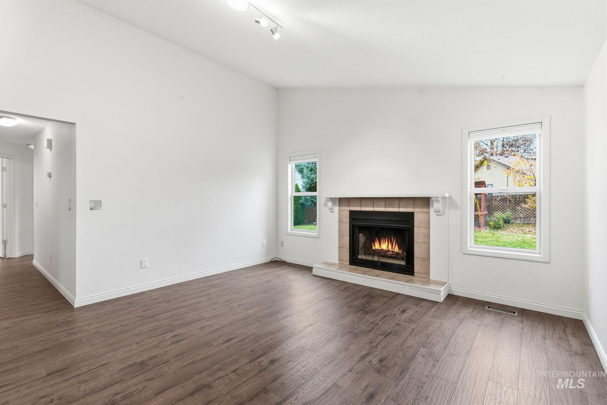 Unfurnished/Staged family room with lofted ceiling, dark wood-style floors, a fireplace, and track lighting
