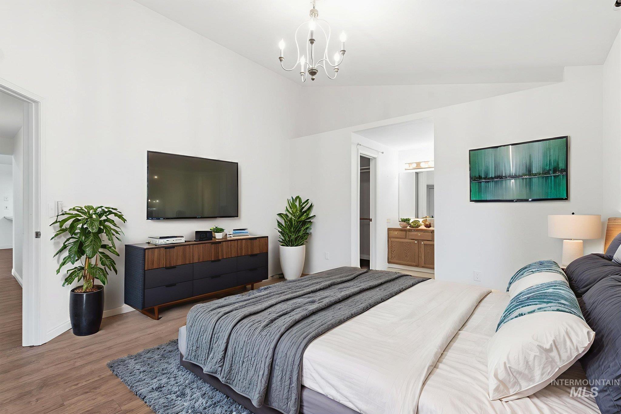 Virtually staged bedroom with lofted ceiling, wood finished floors, a chandelier, and ensuite bath