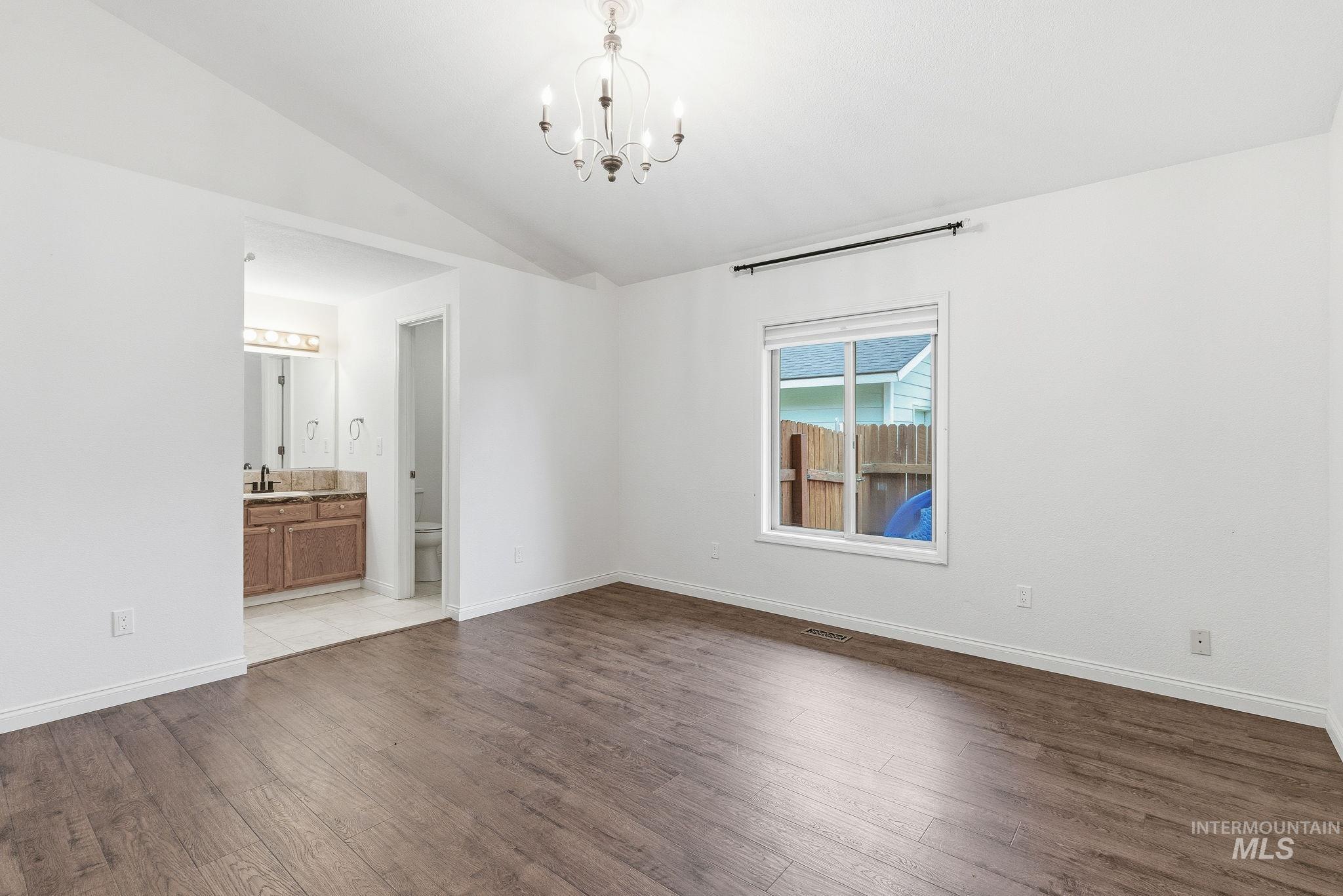 Bedroom with no staging featuring a chandelier, dark wood finished floors, vaulted ceiling, and ensuite bath