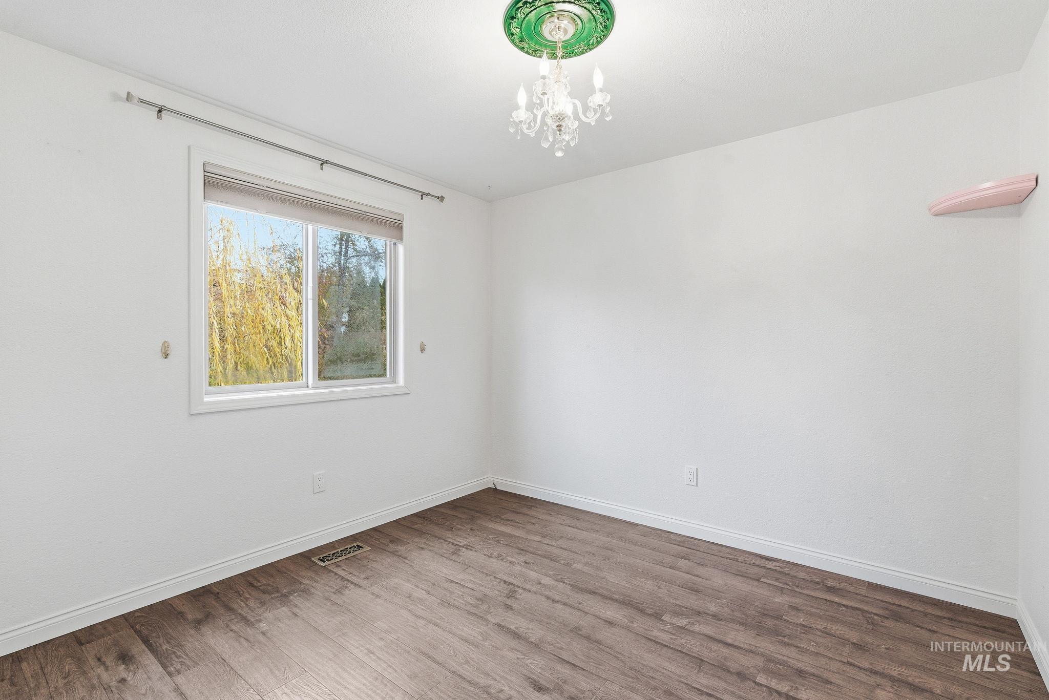 Empty room with wood finished floors and a chandelier