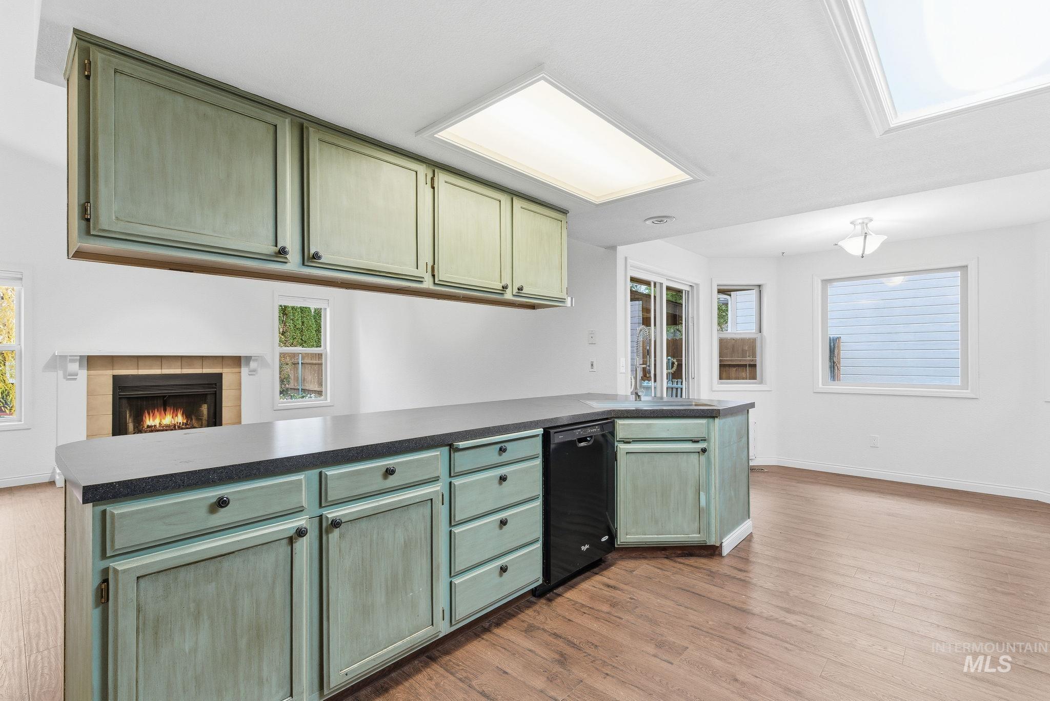 Kitchen featuring green cabinets, dark countertops, a peninsula, and a tiled fireplace