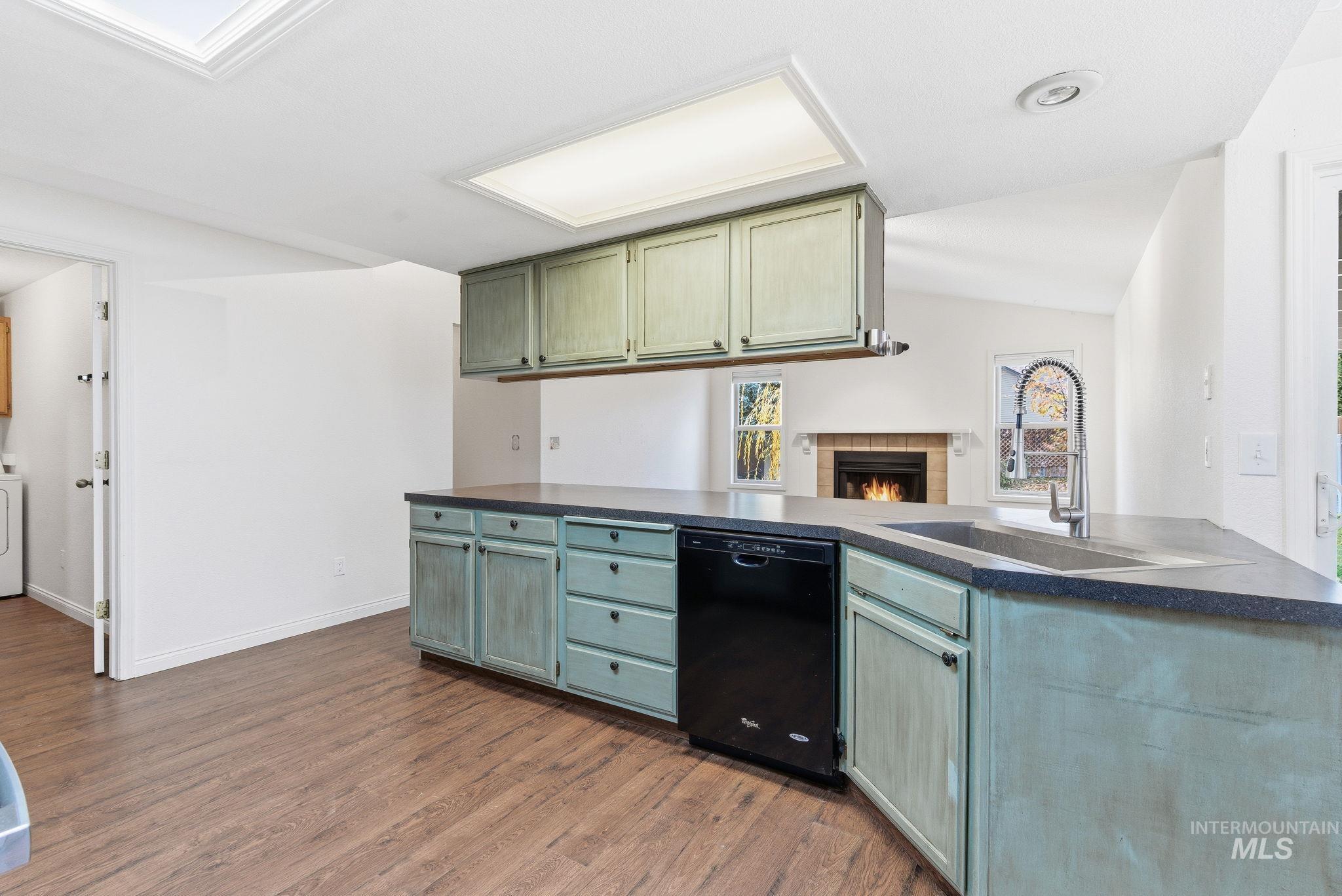 Kitchen with dark countertops, dishwasher, a peninsula, dark wood-style flooring, and vaulted ceiling