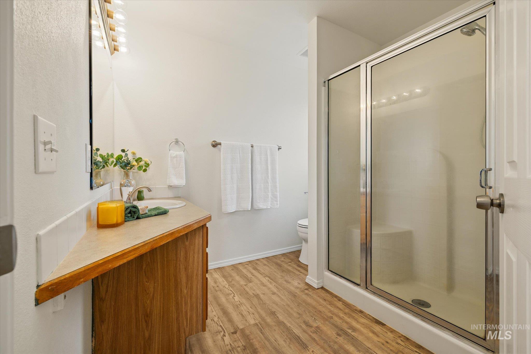 Full bath with light wood-type flooring, vanity, and a shower stall