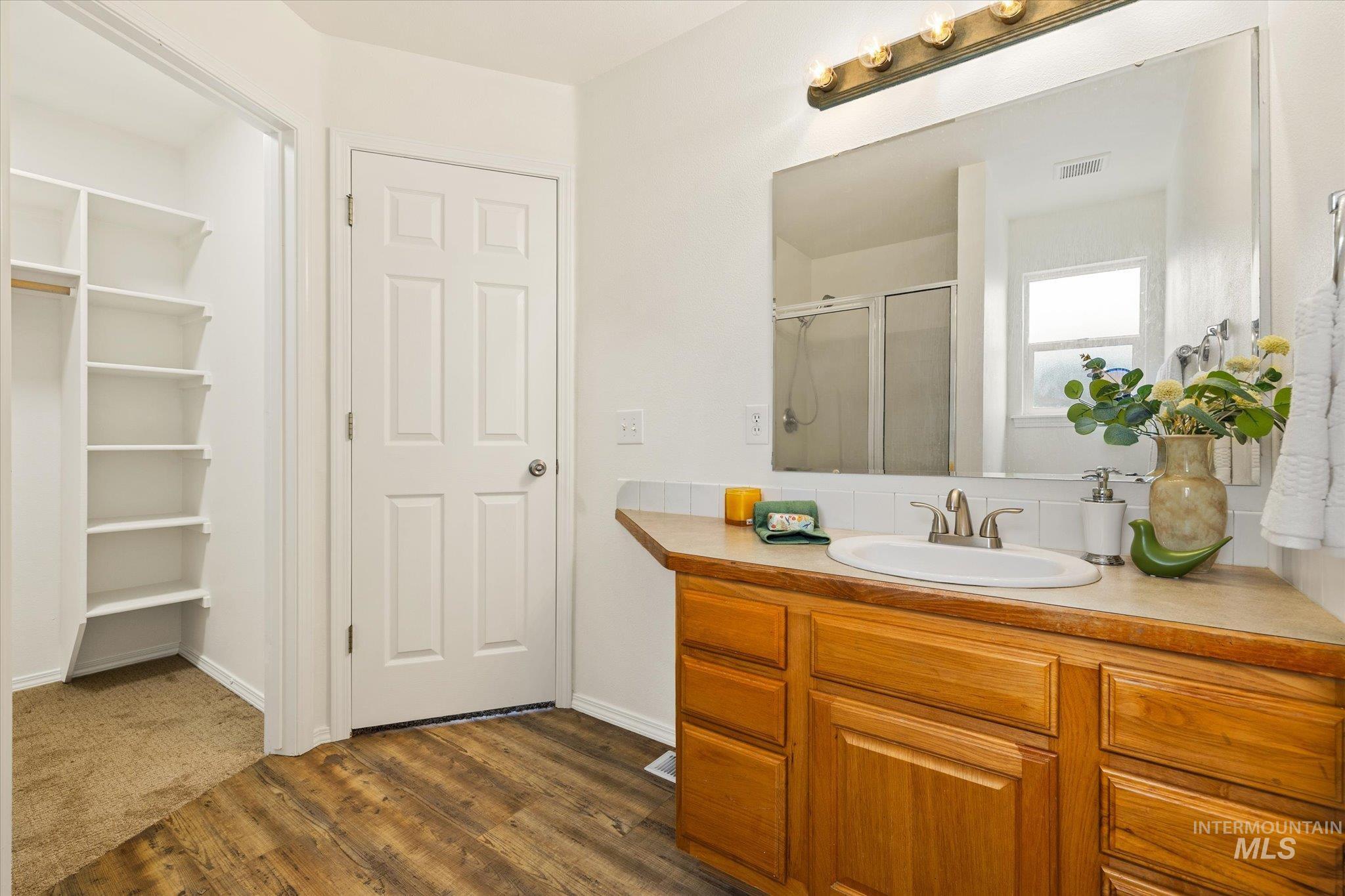 Full bathroom with vanity, a shower stall, dark wood-style floors, and a walk in closet