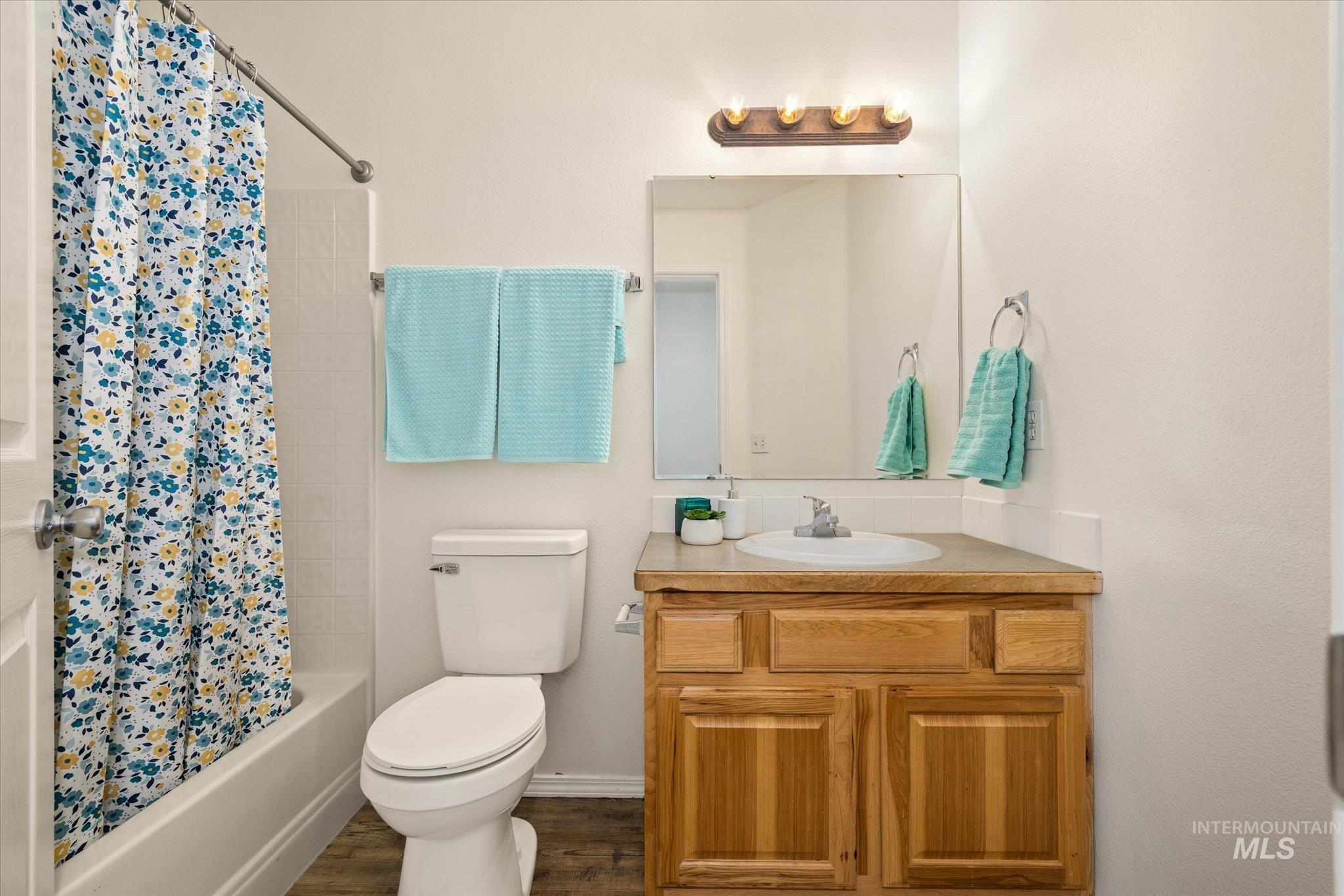 Full bath with shower / tub combo with curtain, vanity, and dark wood finished floors