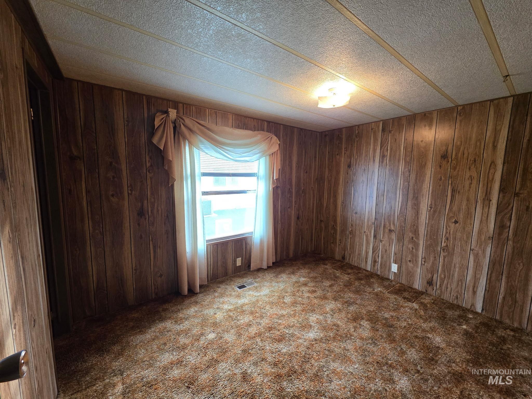Spare room featuring dark colored carpet, wood walls, and a textured ceiling