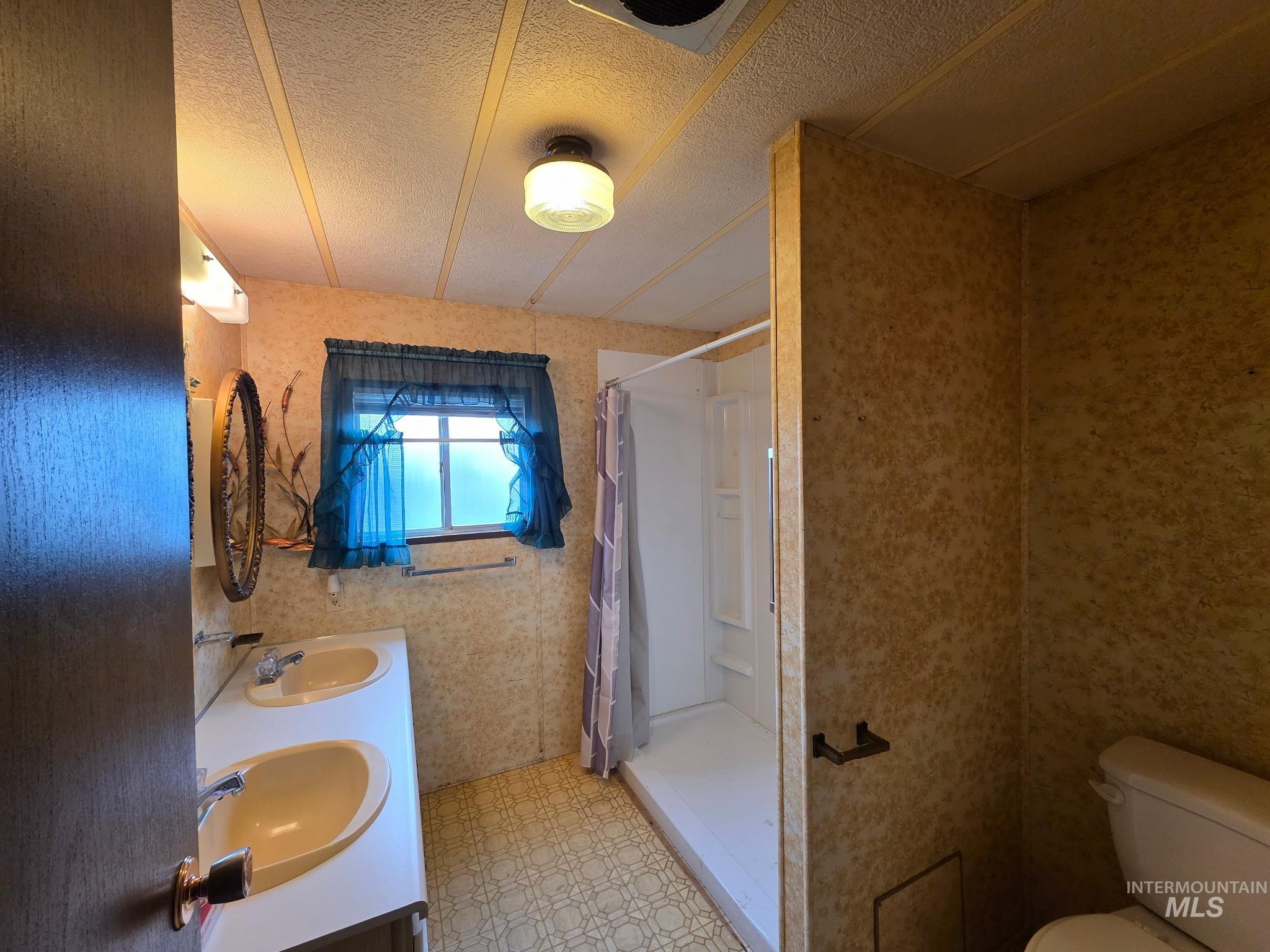 Full bath featuring a stall shower, double vanity, a textured ceiling, and light floors