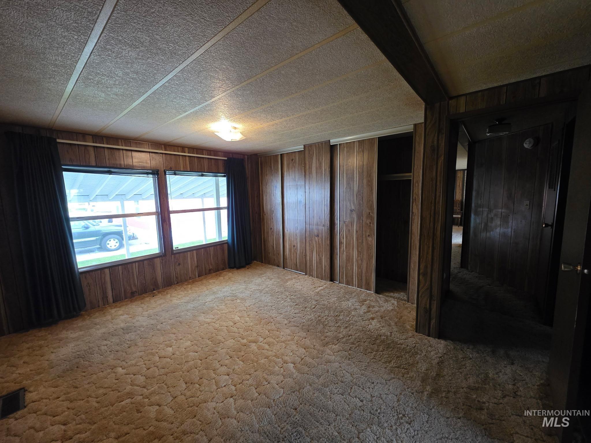 Unfurnished bedroom featuring wood walls, carpet flooring, and multiple closets