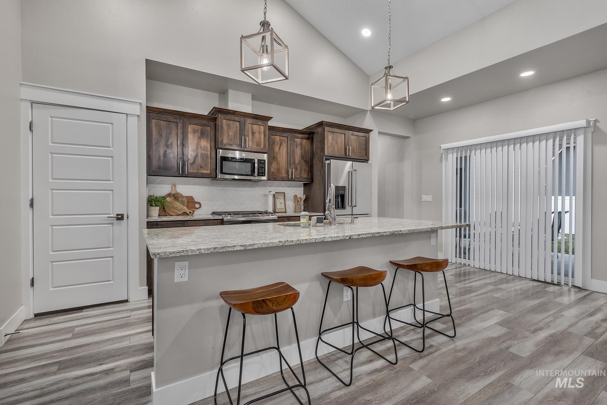 Kitchen with dark brown cabinetry, stainless steel appliances, light wood-style floors, light stone counters, and a breakfast bar area