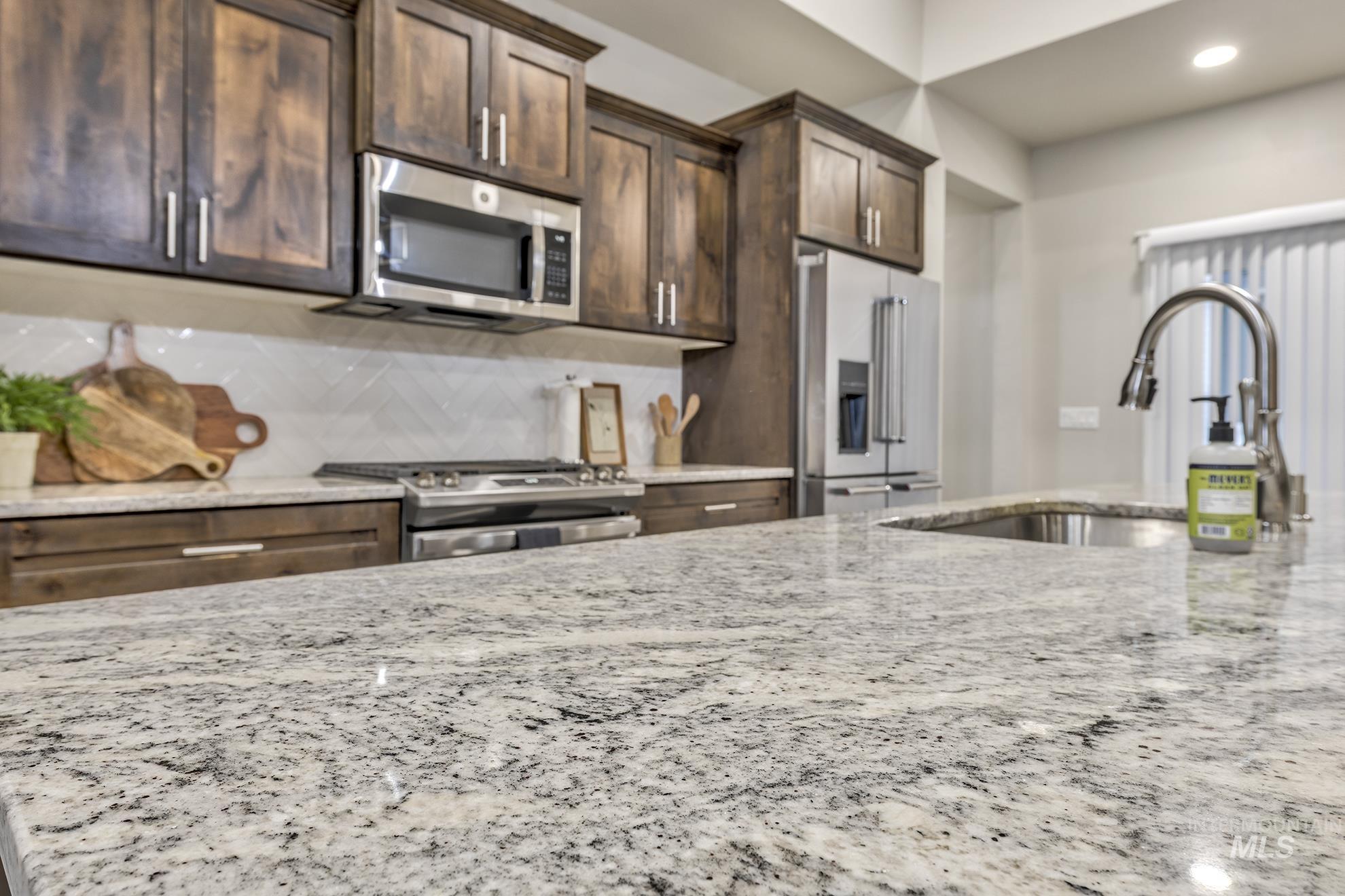 Kitchen with dark brown cabinetry, stainless steel appliances, tasteful backsplash, light stone counters, and recessed lighting