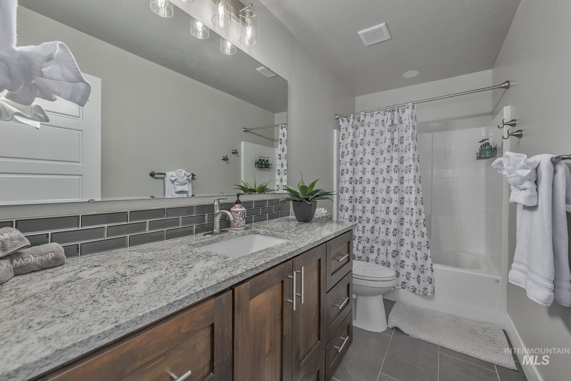 Bathroom featuring dark tile patterned flooring, vanity, shower / tub combo, and backsplash