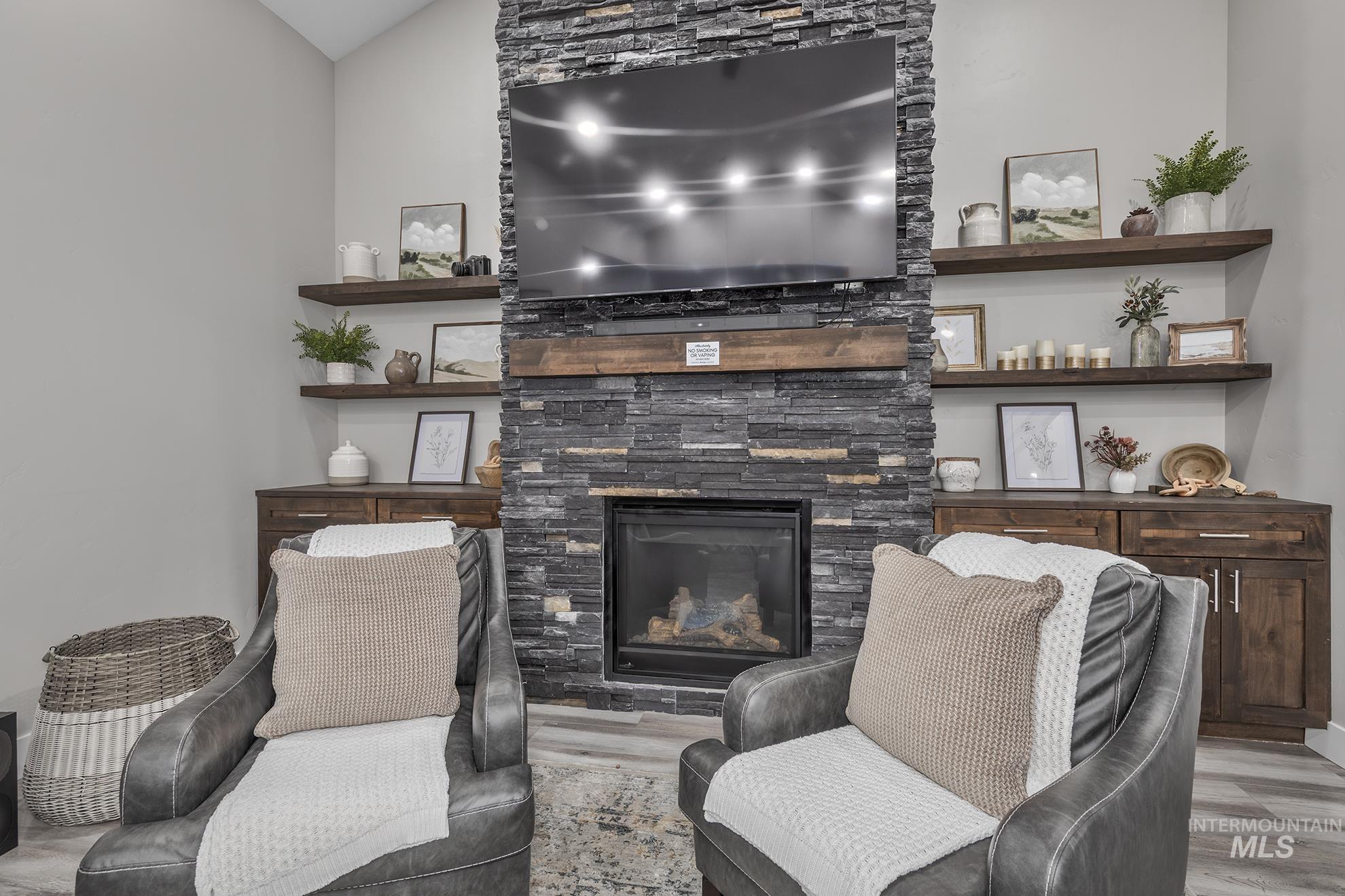 Living room featuring a stone fireplace, wood finished floors, and vaulted ceiling