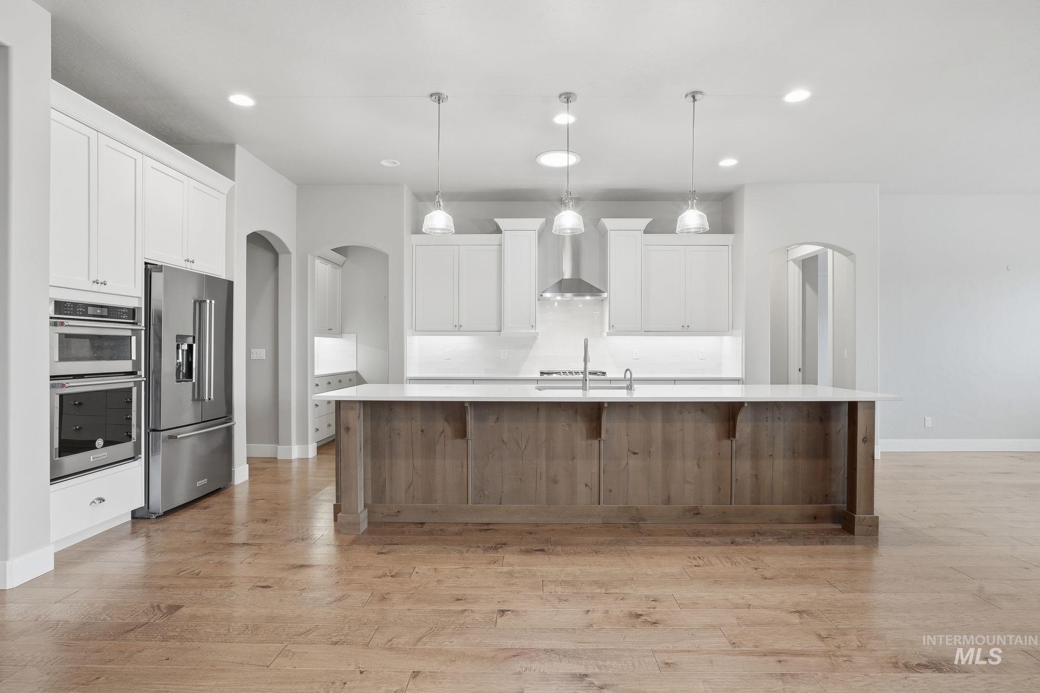 Kitchen with arched walkways, white cabinetry, stainless steel appliances, a spacious island, and recessed lighting