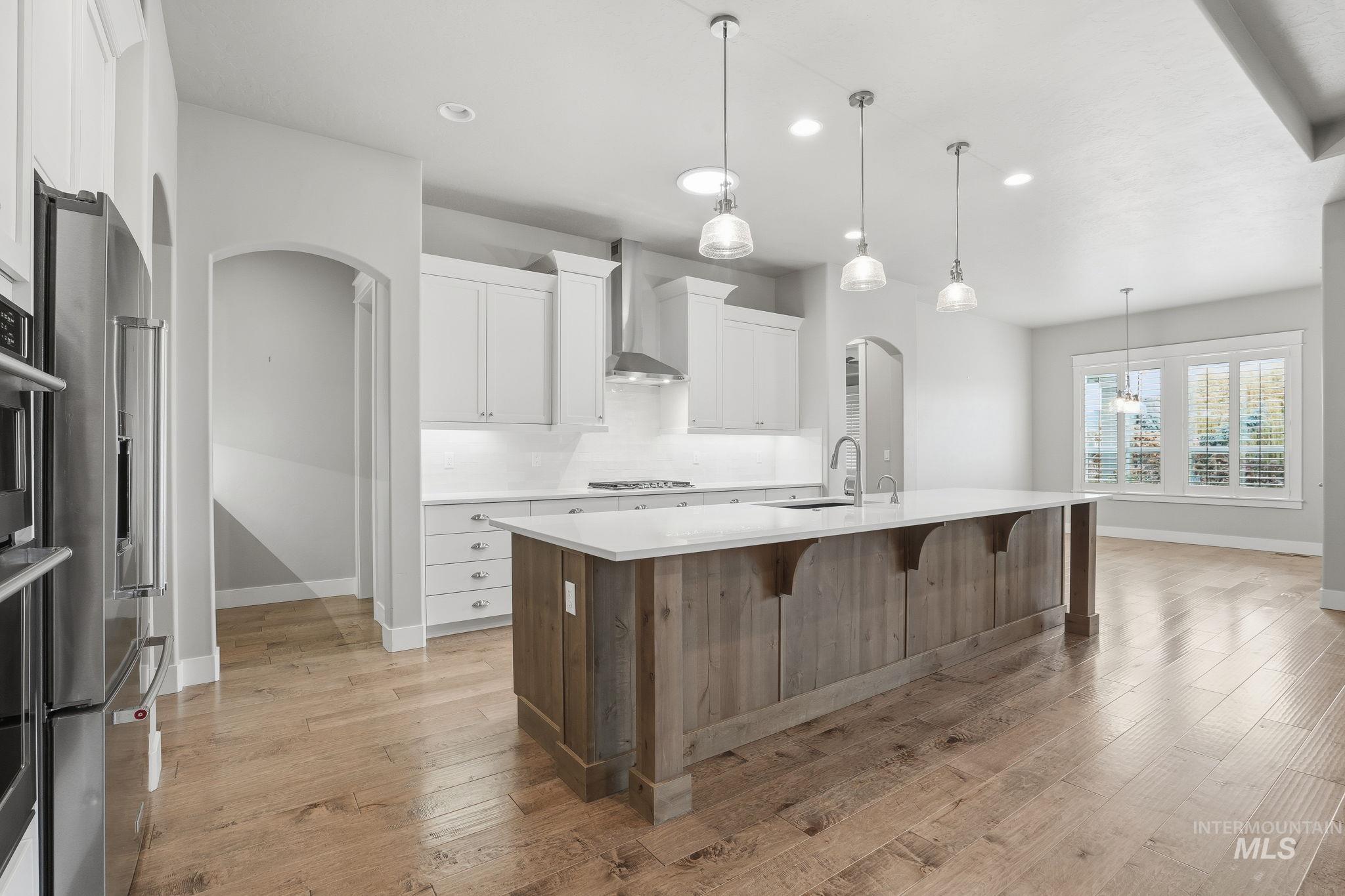 Kitchen featuring arched walkways, white cabinets, backsplash, a breakfast bar, and a kitchen island with sink