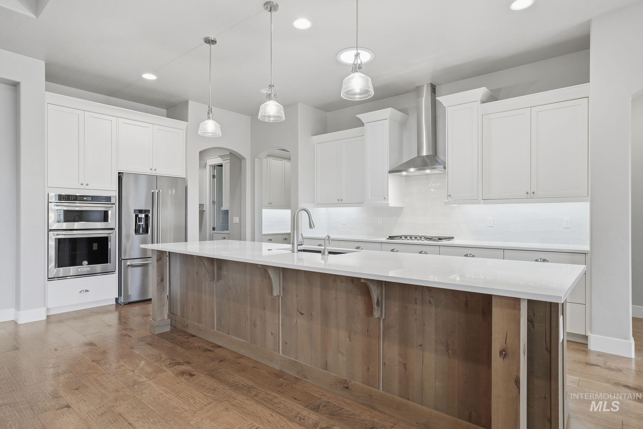 Kitchen with arched walkways, white cabinets, stainless steel appliances, decorative backsplash, and wall chimney range hood