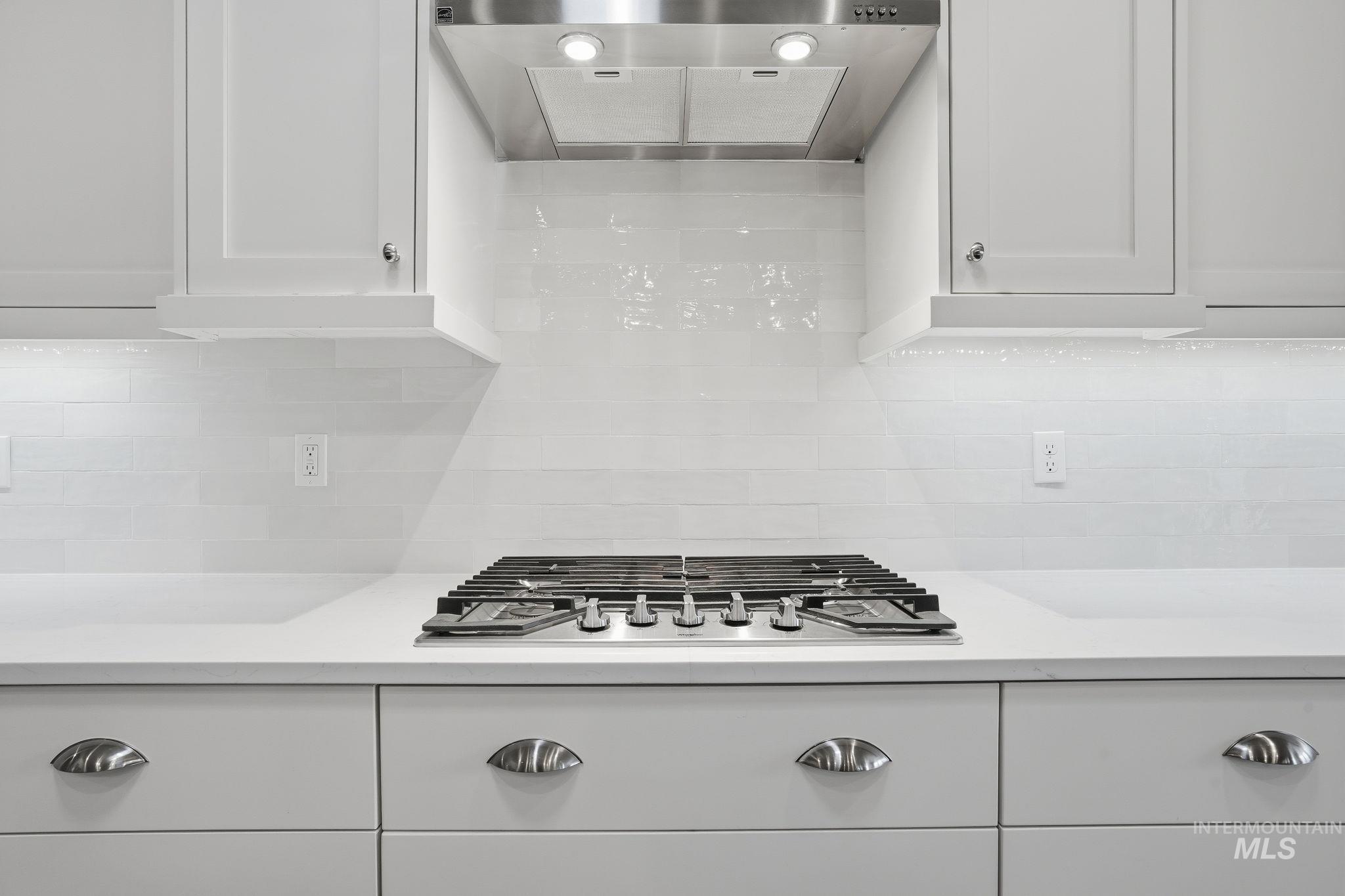 Kitchen with white cabinets, ventilation hood, stainless steel gas stovetop, and tasteful backsplash