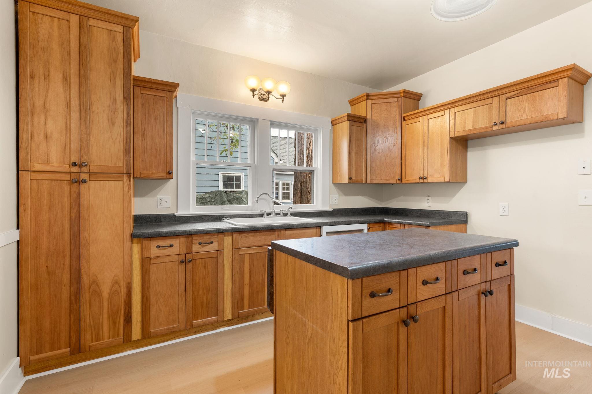 Kitchen with dark countertops, light wood-type flooring, brown cabinetry, a center island, and white dishwasher