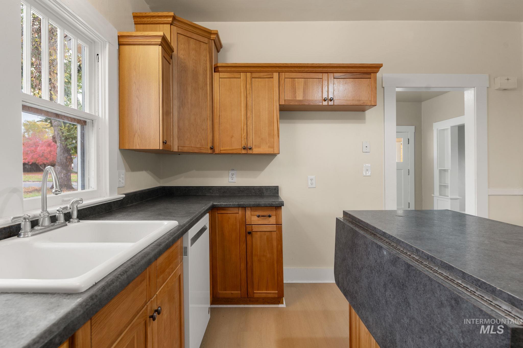 Kitchen with brown cabinets, dark countertops, light wood-type flooring, and dishwashing machine