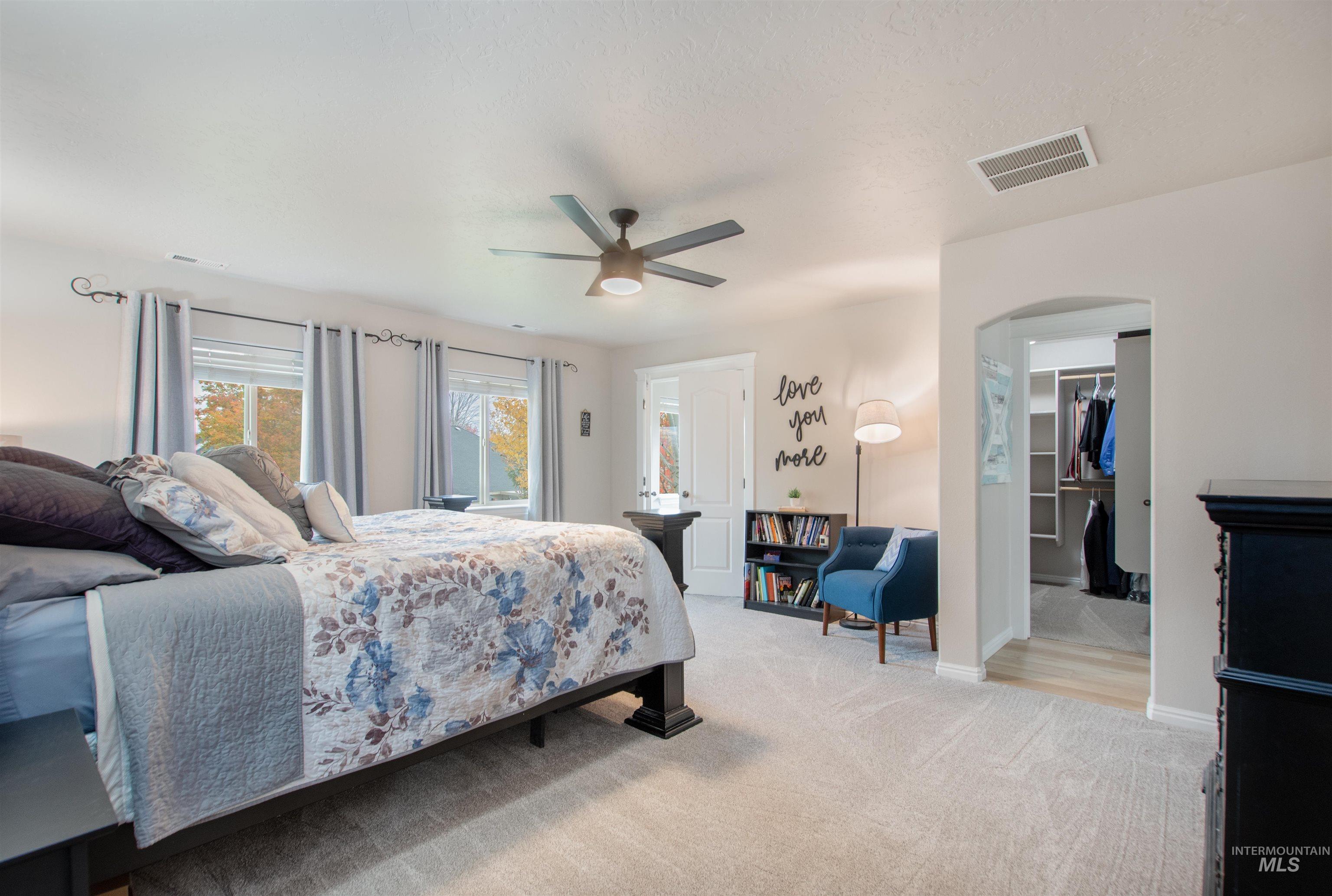 Bedroom with arched walkways, light colored carpet, a walk in closet, and ceiling fan