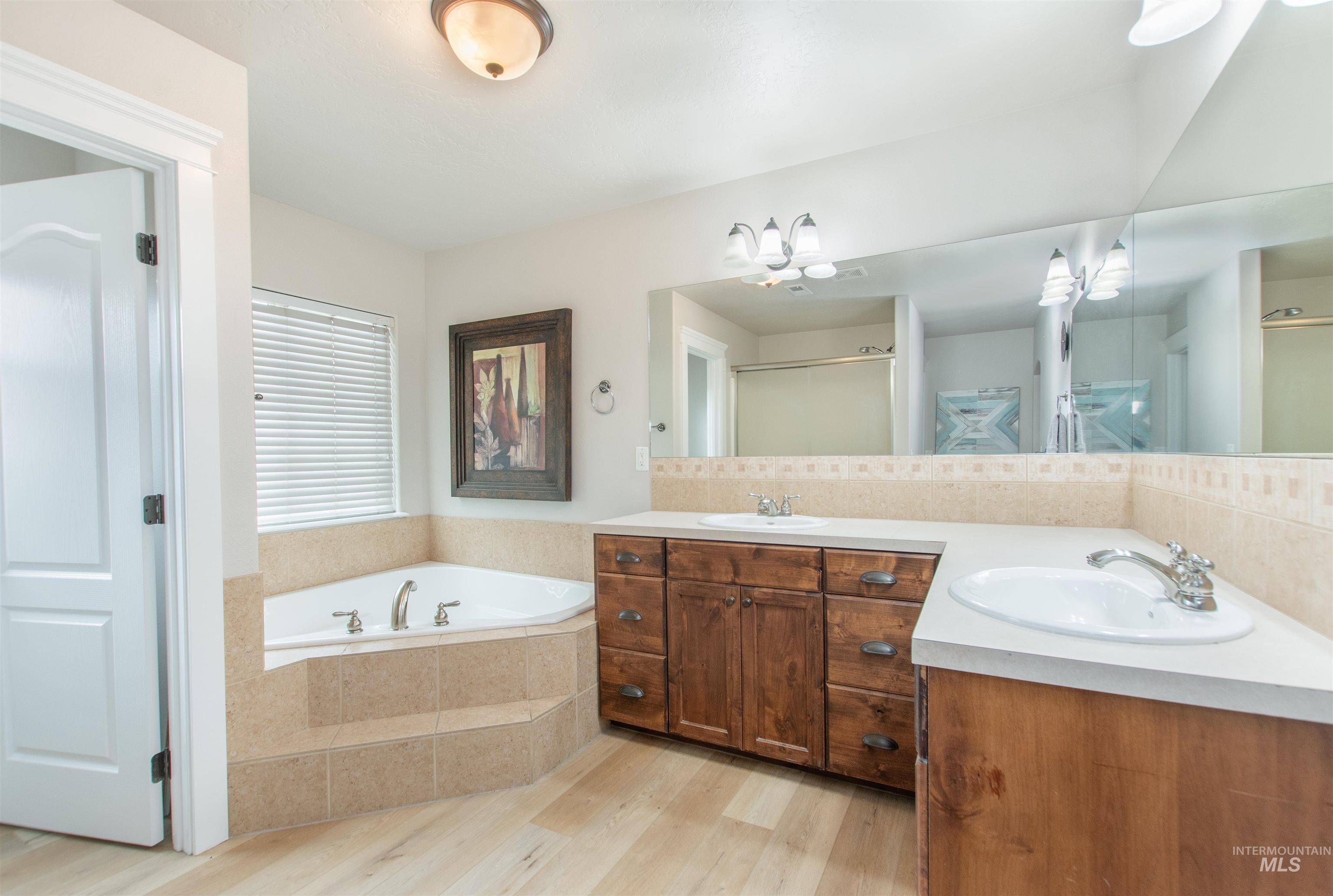 Full bathroom featuring a bath, light wood-style floors, double vanity, and a shower stall