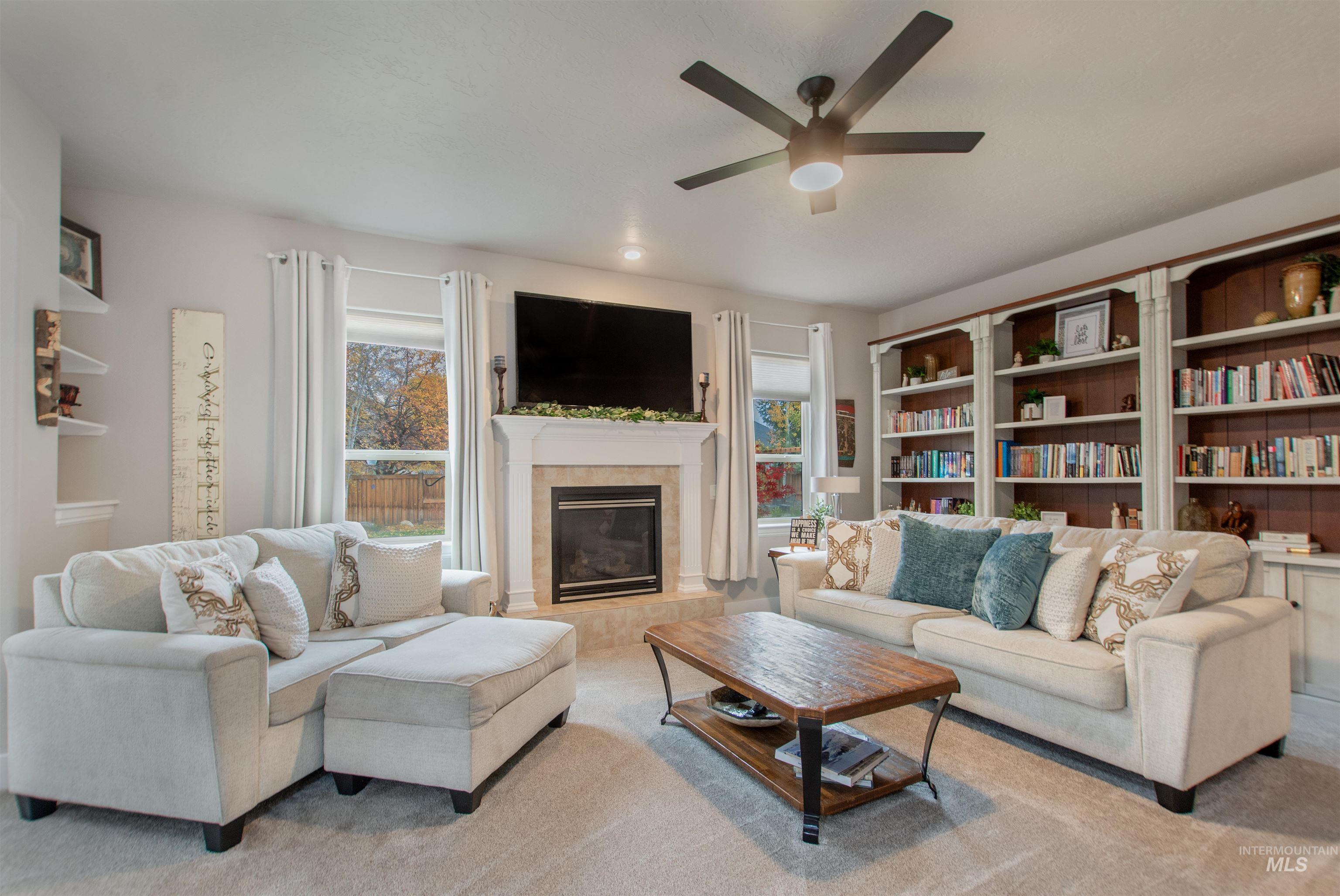 Carpeted living room with plenty of natural light, a tile fireplace, and ceiling fan