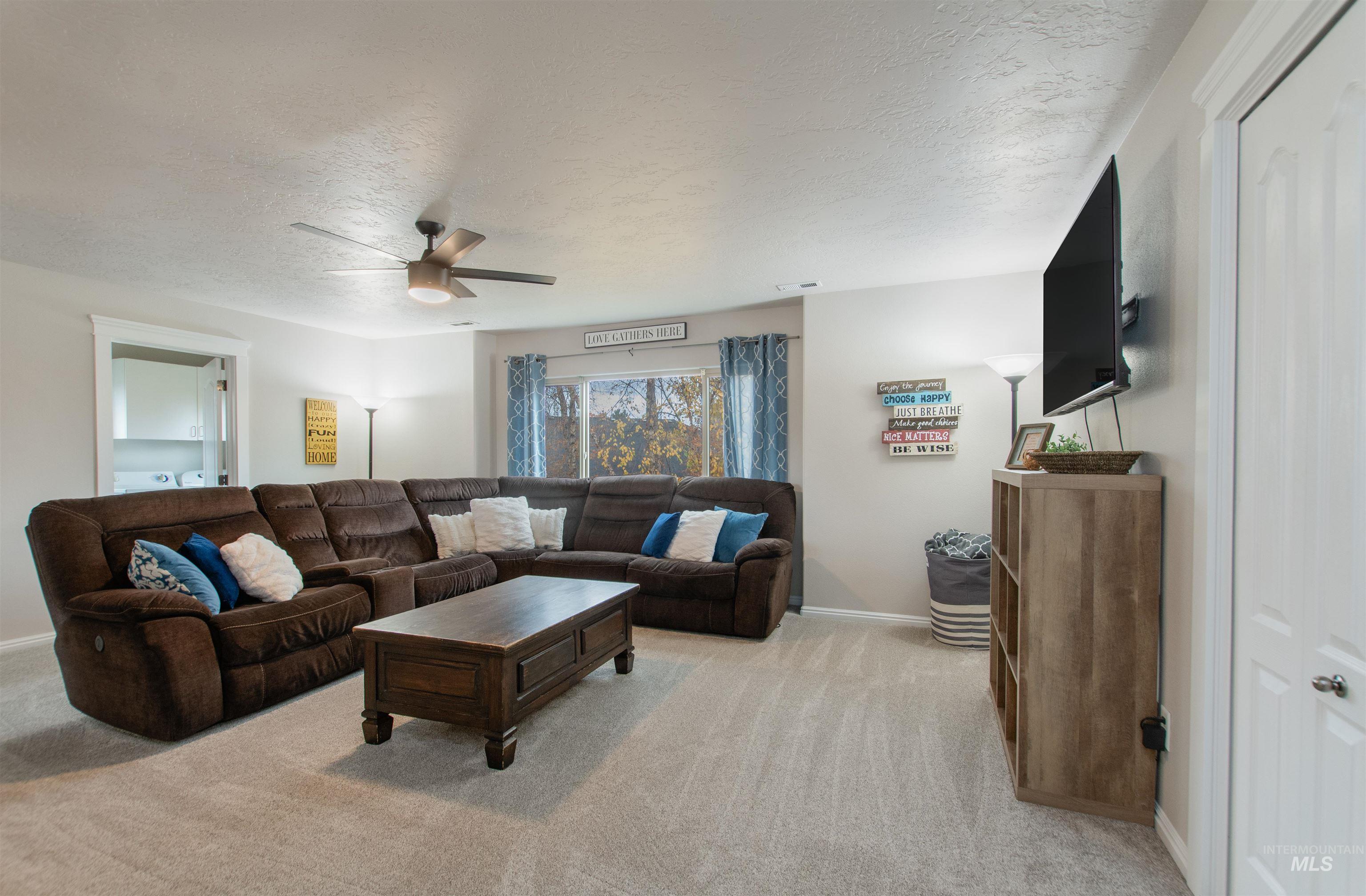 Living room with a textured ceiling, light colored carpet, and ceiling fan