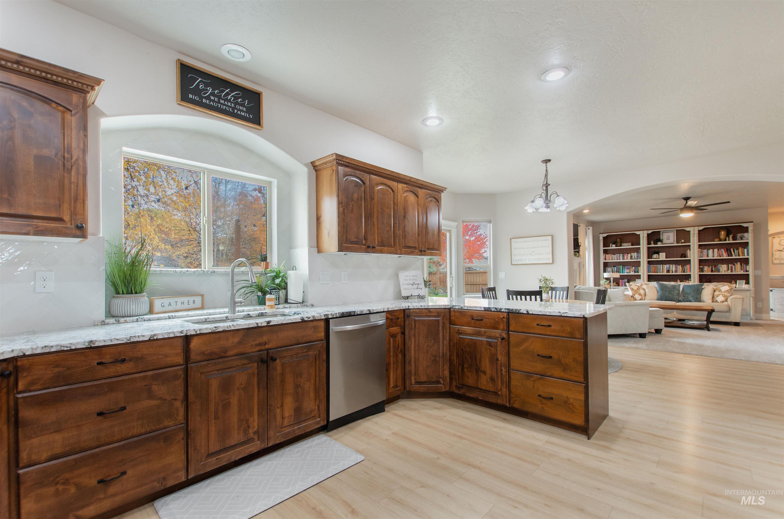 Kitchen featuring decorative light fixtures, light stone counters, dishwasher, ceiling fan, and light wood-style flooring