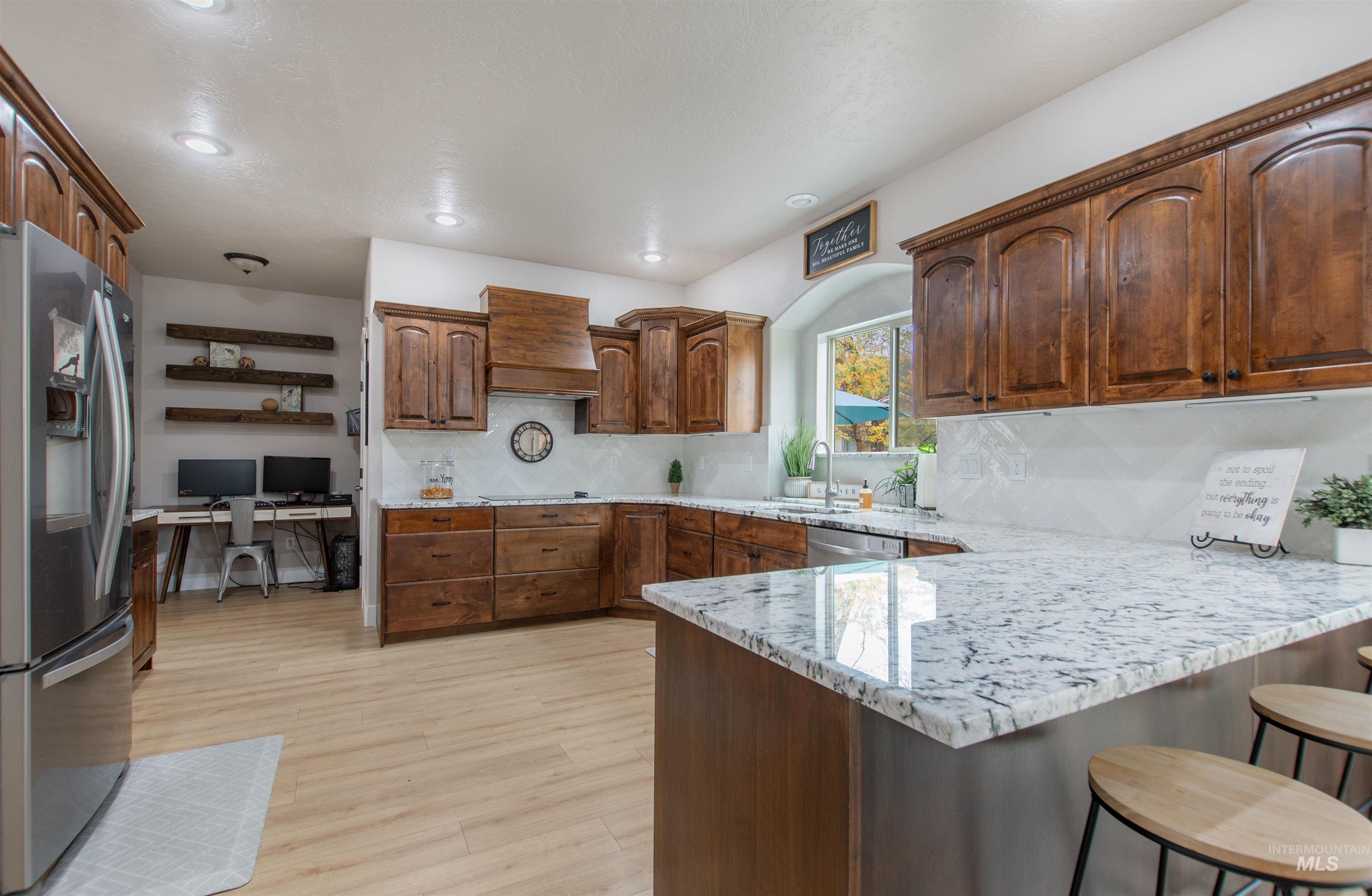 Kitchen featuring appliances with stainless steel finishes, a peninsula, a kitchen breakfast bar, light stone counters, and backsplash