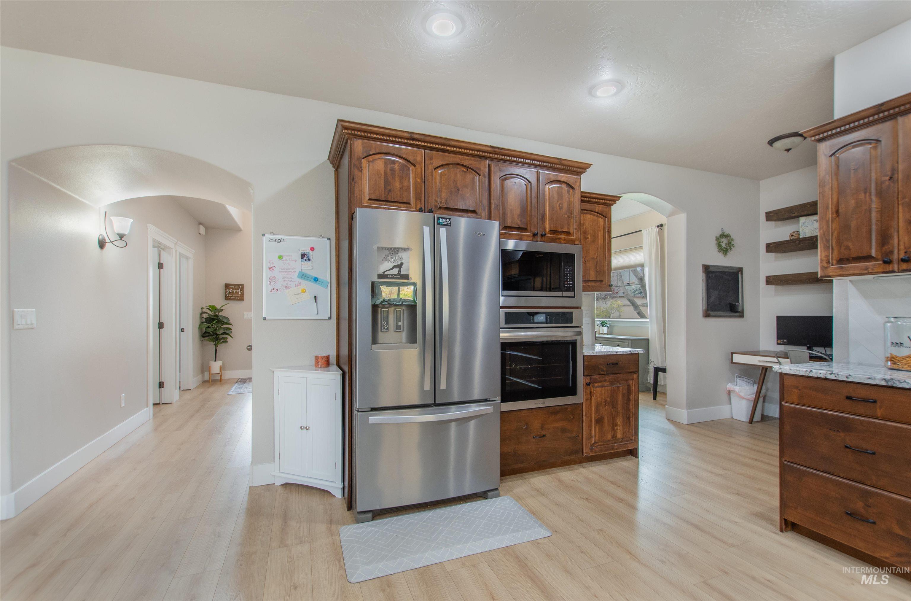 Kitchen featuring arched walkways, appliances with stainless steel finishes, light wood finished floors, open shelves, and light stone counters