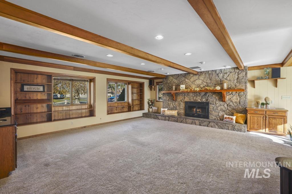 Unfurnished living room featuring beamed ceiling, carpet floors, and a stone fireplace