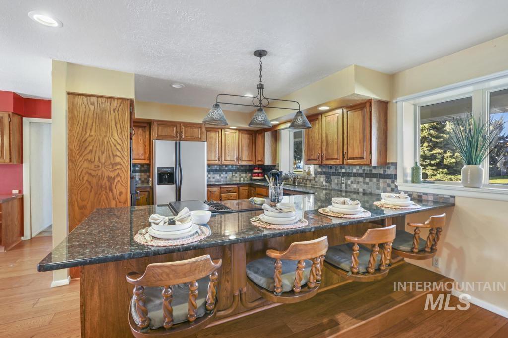 Kitchen featuring brown cabinetry, stainless steel refrigerator with ice dispenser, dark stone countertops, decorative backsplash, and recessed lighting