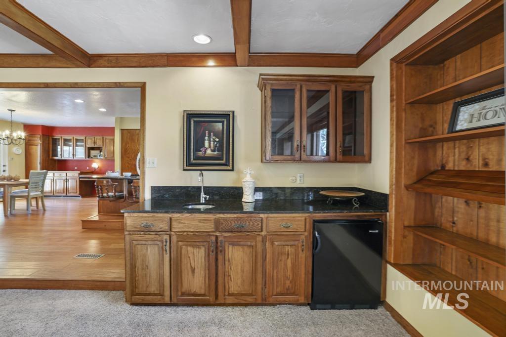 Bar with brown cabinetry, dark stone countertops, beamed ceiling, glass insert cabinets, and recessed lighting