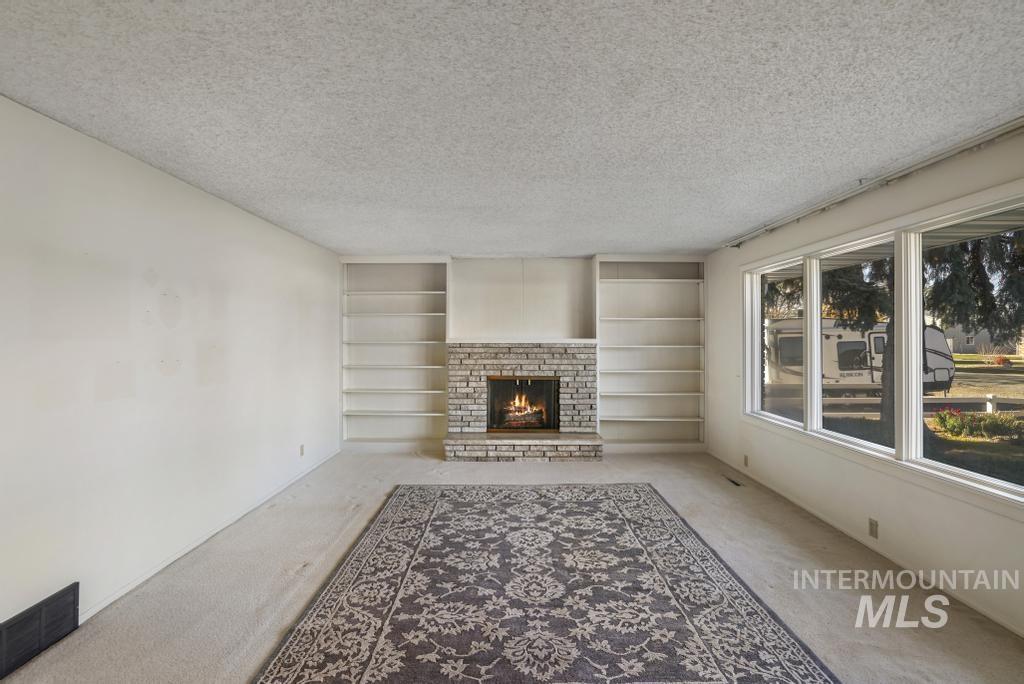 Unfurnished living room featuring carpet floors, a textured ceiling, a brick fireplace, and built in features