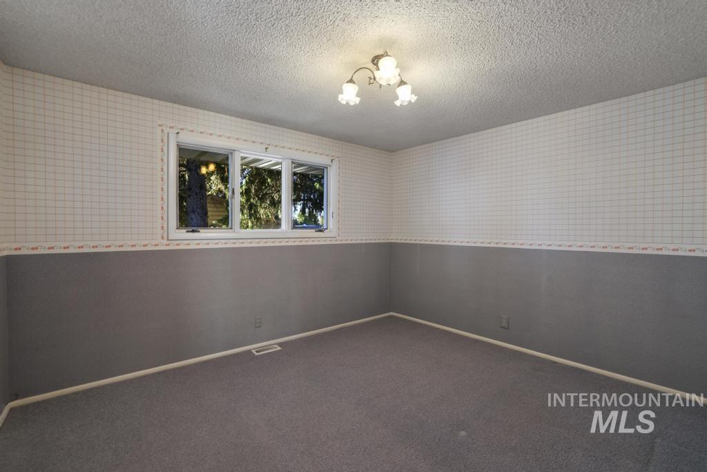 Carpeted empty room featuring a textured ceiling, a chandelier, and wallpapered walls