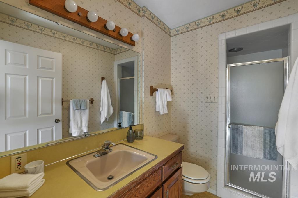 Bathroom featuring a stall shower, vanity, and wallpapered walls