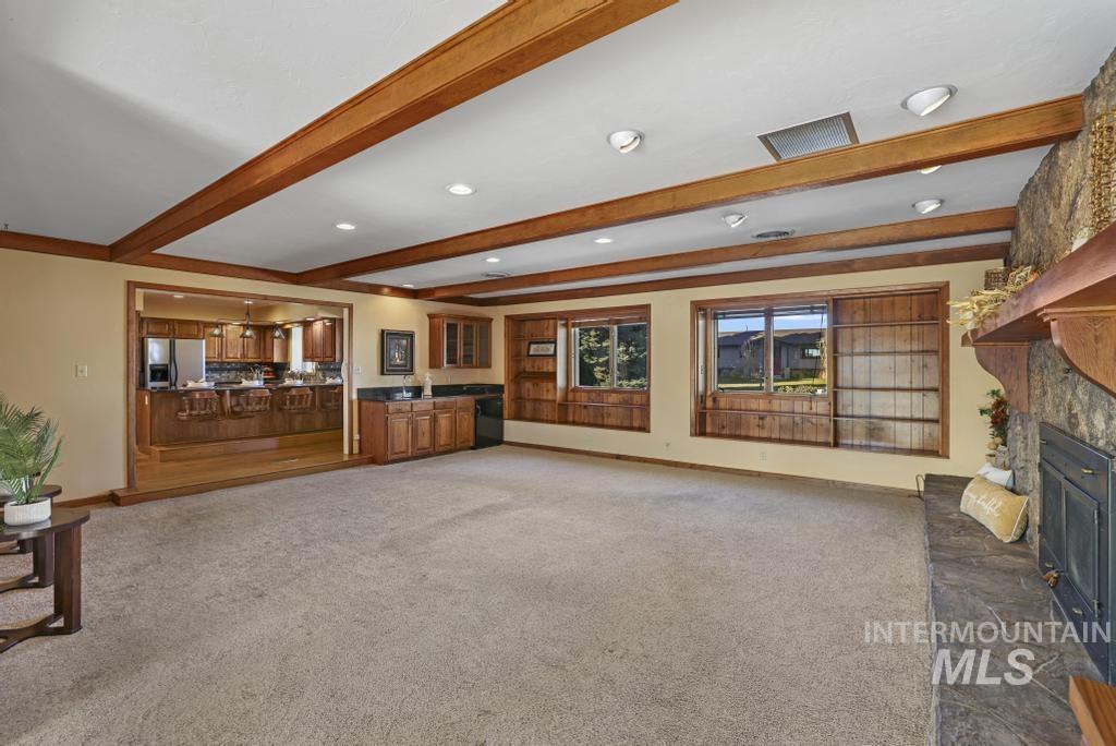 Unfurnished living room with beam ceiling, dark carpet, a fireplace with raised hearth, and recessed lighting
