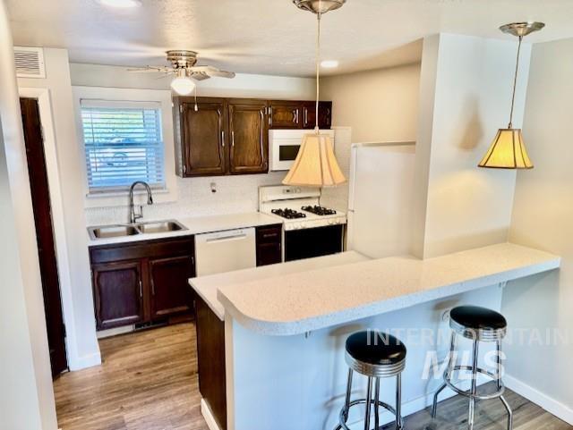 Kitchen with a kitchen bar, light countertops, dark brown cabinets, a peninsula, and light wood-style flooring