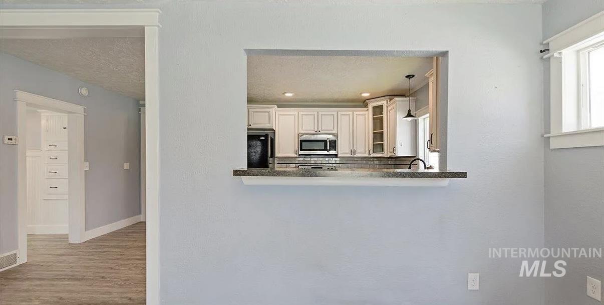 Kitchen featuring glass insert cabinets, stainless steel microwave, fridge, hanging light fixtures, and wood finished floors