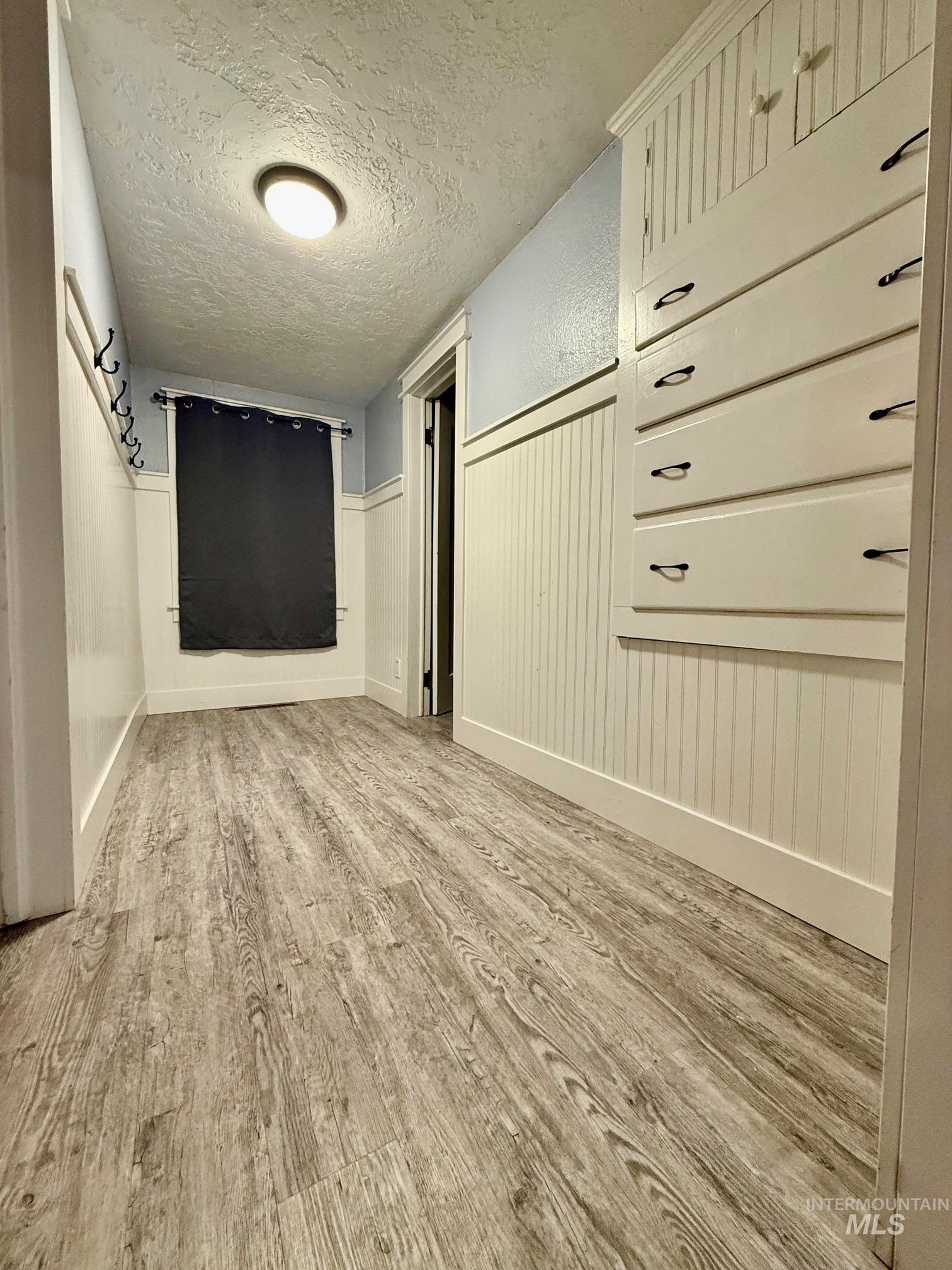 Hallway featuring wainscoting, a textured ceiling, and light wood-type flooring