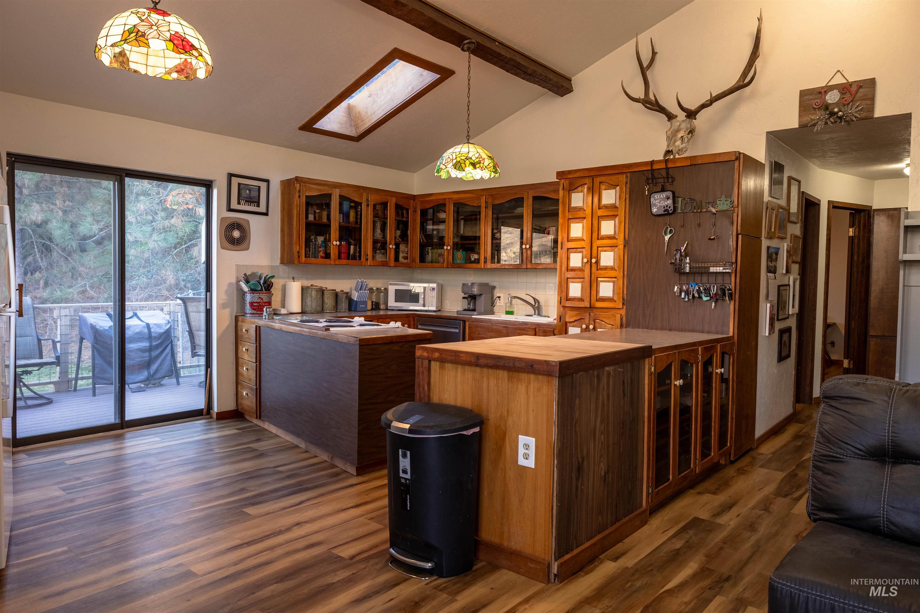 Kitchen featuring glass insert cabinets, brown cabinets, beamed ceiling, high vaulted ceiling, and pendant lighting