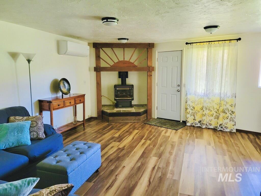 Living area with a wood stove, a textured ceiling, wood finished floors, and an AC wall unit