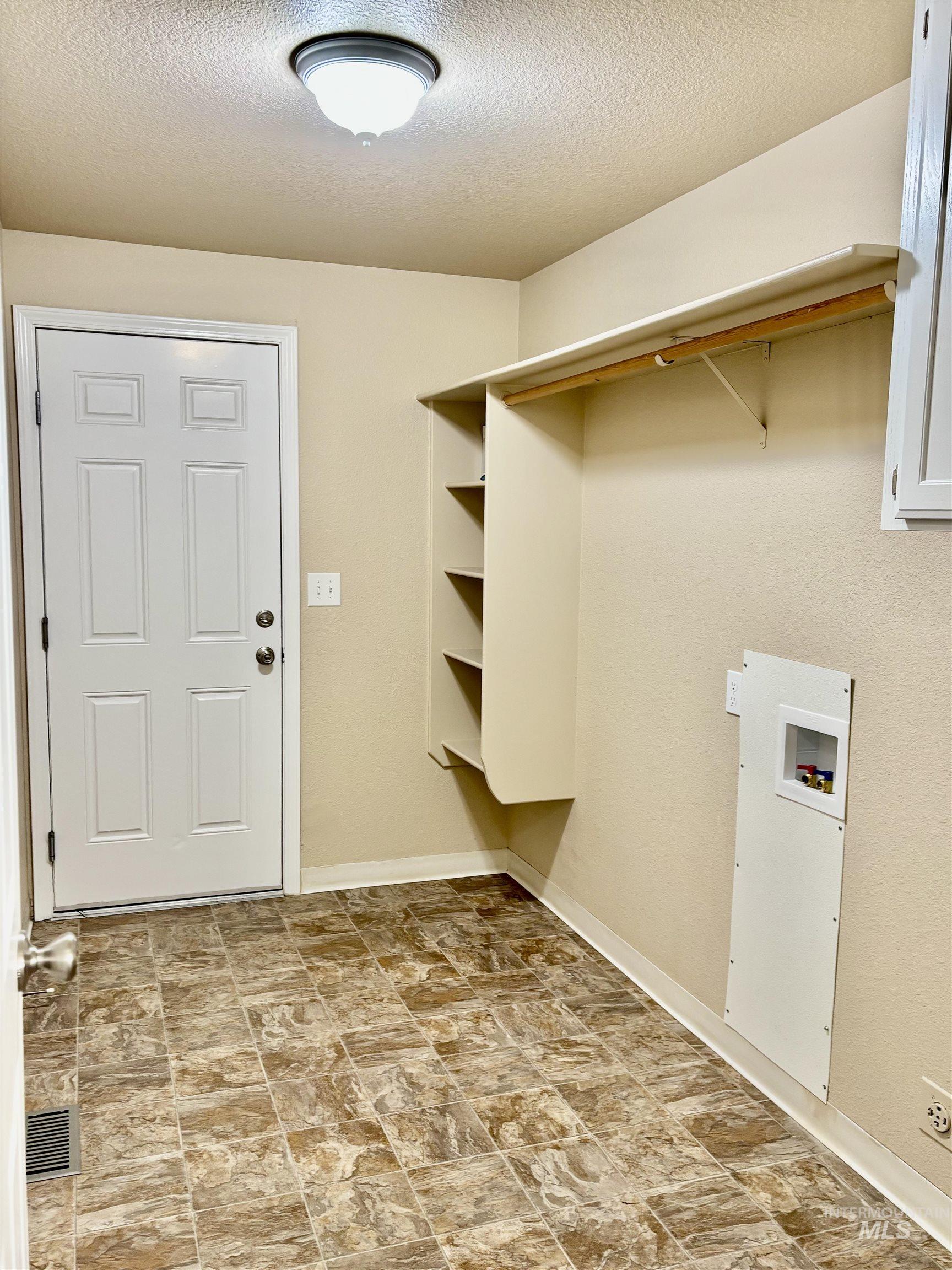 Washroom with a textured ceiling, hookup for a washing machine, and stone finish flooring