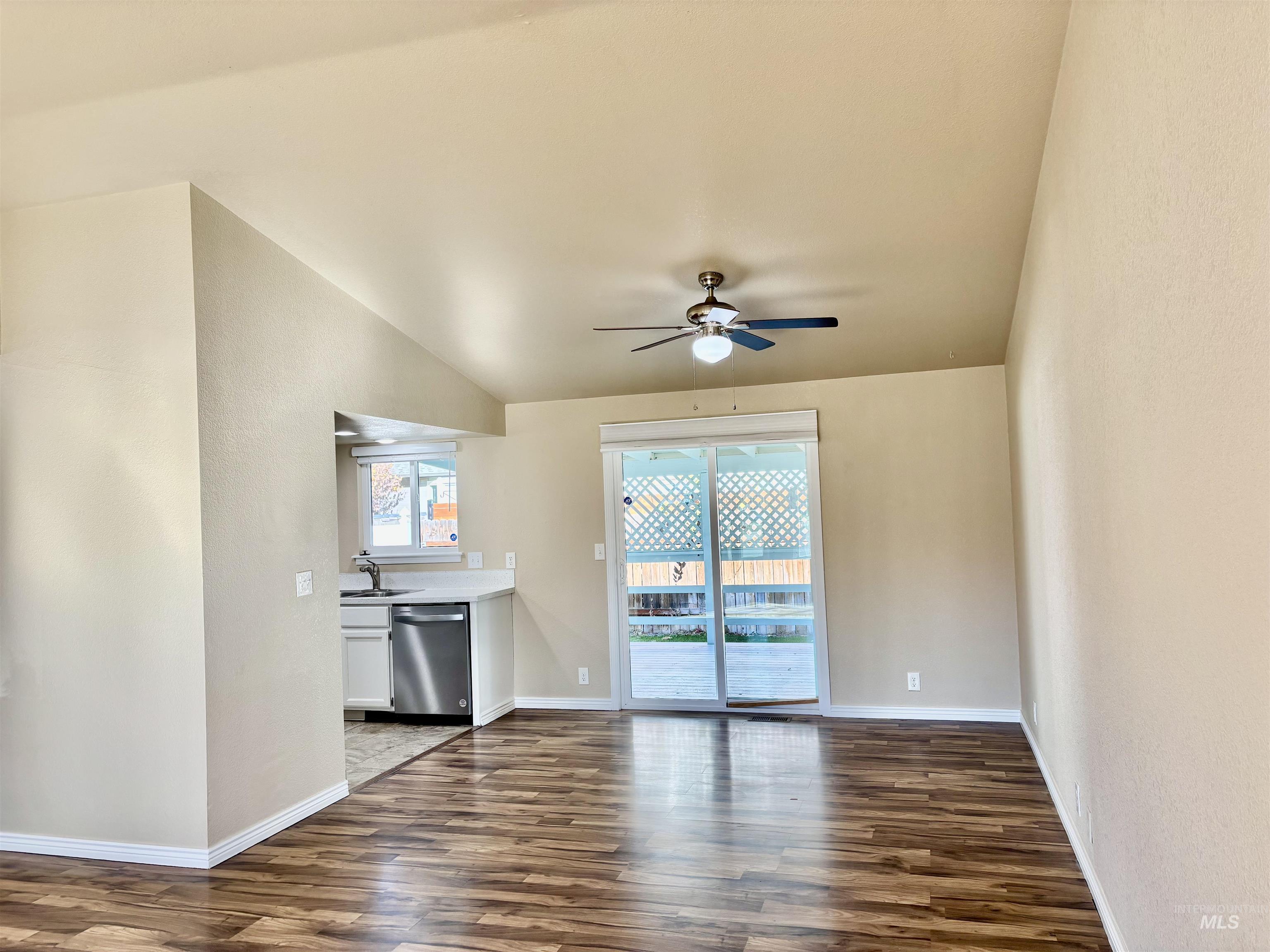 Spare room featuring dark wood-type flooring, a ceiling fan, a textured wall, and lofted ceiling