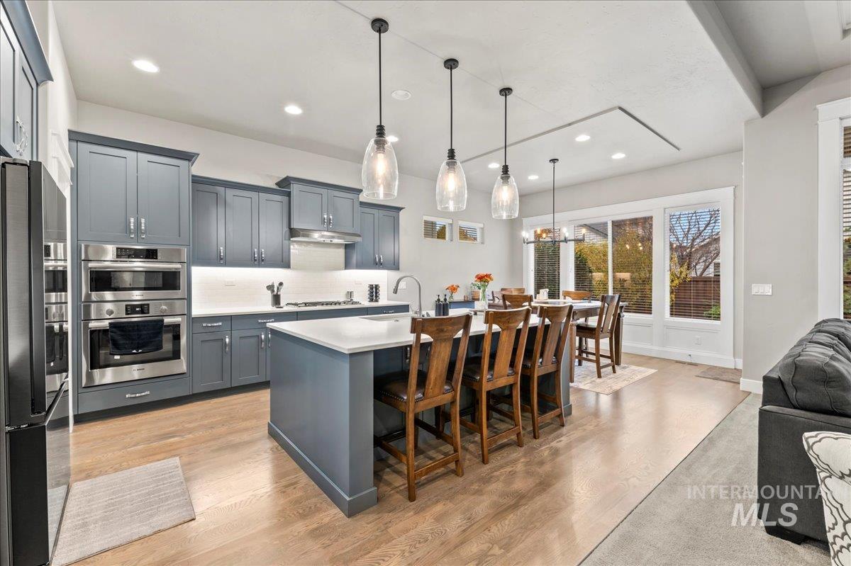 Kitchen featuring a breakfast bar, backsplash, stainless steel appliances, hanging light fixtures, and a center island with sink