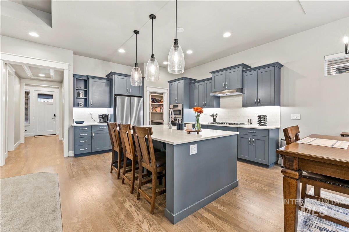 Kitchen featuring pendant lighting, tasteful backsplash, a kitchen island with sink, light wood finished floors, and a kitchen breakfast bar