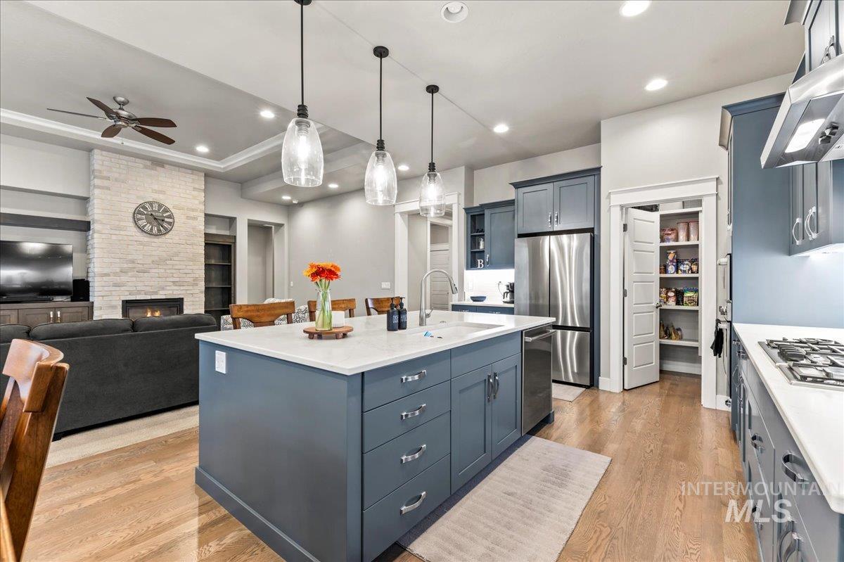 Kitchen featuring decorative light fixtures, light wood-style floors, appliances with stainless steel finishes, a kitchen island with sink, and a fireplace