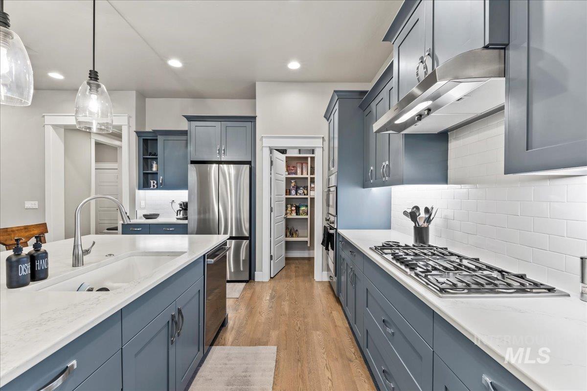 Kitchen with stainless steel appliances, light wood-style floors, light stone countertops, hanging light fixtures, and recessed lighting